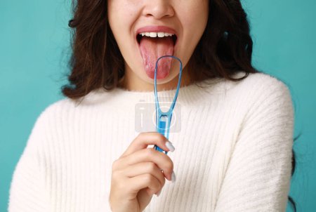 Téléchargez les photos : Jeune femme asiatique avec grattoir de langue sur fond bleu - en image libre de droit