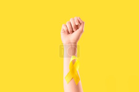 Woman with yellow awareness ribbon on color background, closeup