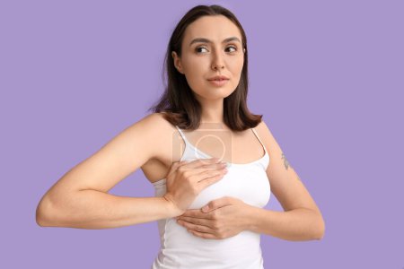 Junge Frau überprüft ihre Brust auf fliederfarbenem Hintergrund. Krebsaufklärungskonzept