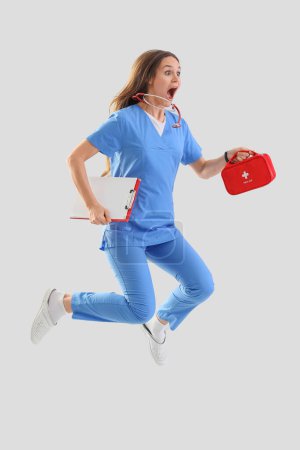 Schockierte Ärztin mit Verbandskasten und Klemmbrett springt auf hellem Hintergrund