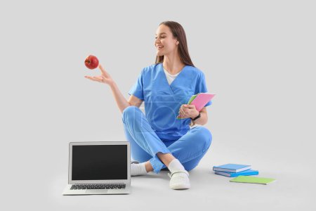 Interna médica femenina con manzana estudiando sobre fondo claro