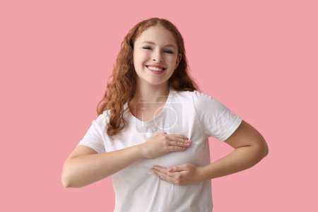 Junge Frau überprüft ihre Brust auf rosa Hintergrund. Krebsaufklärungskonzept
