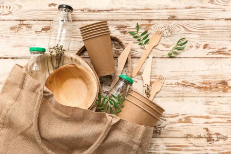 Foto de Vajilla ecológica con botellas de vidrio, ramas de plantas y bolsa sobre fondo de madera marrón - Imagen libre de derechos