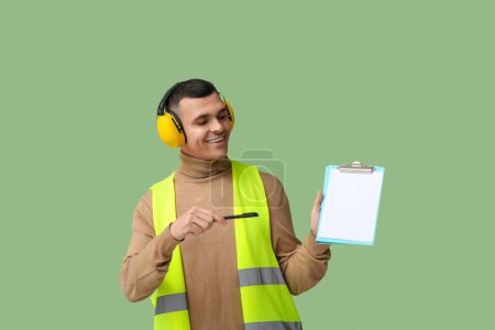 Foto de Joven ingeniero masculino apuntando al portapapeles con papel en blanco sobre fondo verde - Imagen libre de derechos