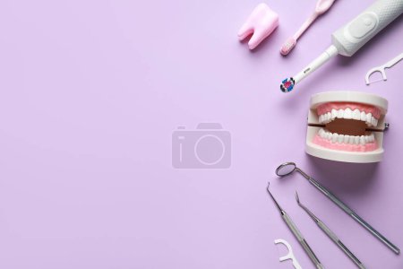 Foto de Herramientas dentales, suministros de higiene bucal y modelo de mandíbula sobre fondo lila. Día Mundial del Dentista - Imagen libre de derechos