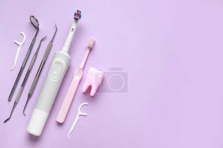 Foto de Cepillos de dientes, herramientas dentales, modelo de dientes y mondadientes de hilo dental sobre fondo lila. Día Mundial del Dentista - Imagen libre de derechos