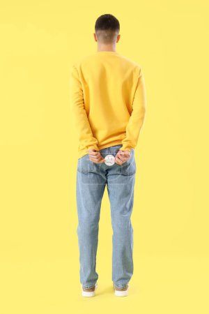 Foto de Hombre joven con hemorroides y sonrisa triste sobre fondo amarillo, vista trasera - Imagen libre de derechos