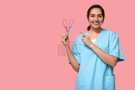 Téléchargez les photos : Jeune dentiste féminine avec grattoirs de langue sur fond rose - en image libre de droit