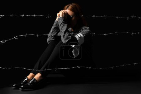 Mature Jewish woman sitting behind barbed wire on black background. International Holocaust Remembrance Day