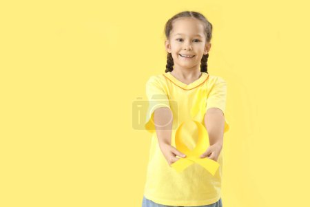 Téléchargez les photos : Jolie petite fille avec des rubans jaunes sur fond de couleur. Concept de sensibilisation au cancer chez l'enfant - en image libre de droit