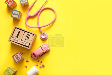 Téléchargez les photos : Calendrier avec date de la journée de sensibilisation au cancer chez l'enfant, stéthoscope et jouets sur fond jaune - en image libre de droit