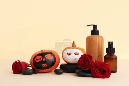 Foto de Calabazas con caras dibujadas, máscaras de barro, suministros de spa y rosas sobre fondo beige - Imagen libre de derechos