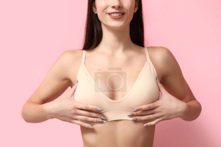 Téléchargez les photos : Jeune femme vérifiant son sein sur fond rose - en image libre de droit