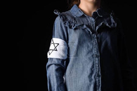 Little Jewish girl with armband on black background, closeup. International Holocaust Remembrance Day