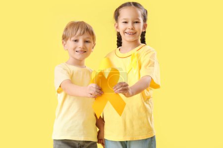 Téléchargez les photos : Petits enfants mignons avec des rubans jaunes sur fond de couleur. Concept de sensibilisation au cancer chez l'enfant - en image libre de droit