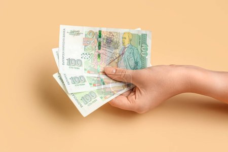 Mano femenina sosteniendo billetes de lev búlgaros sobre fondo beige