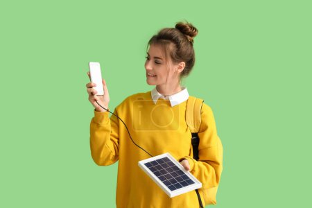 Foto de Mujer bastante joven cargando teléfono móvil con panel solar portátil sobre fondo verde - Imagen libre de derechos