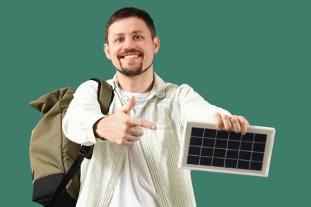 Foto de Hombre guapo apuntando al panel solar portátil sobre fondo verde - Imagen libre de derechos