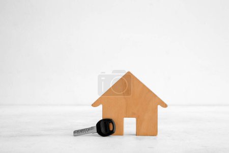 Téléchargez les photos : Figurine de maison en bois avec clé sur table blanche grunge près du mur. Concept d'achat immobilier - en image libre de droit