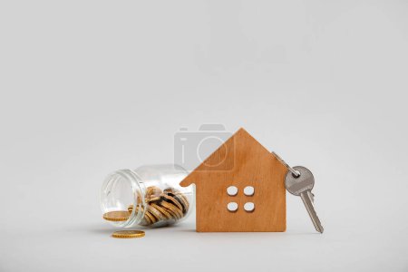Téléchargez les photos : Figurine de maison en bois avec argent et clé sur fond gris. Concept d'achat immobilier - en image libre de droit