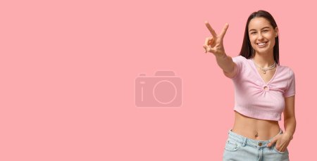 Téléchargez les photos : Sexy jeune femme avec piercing nombril montrant geste de victoire sur fond rose avec espace pour le texte - en image libre de droit