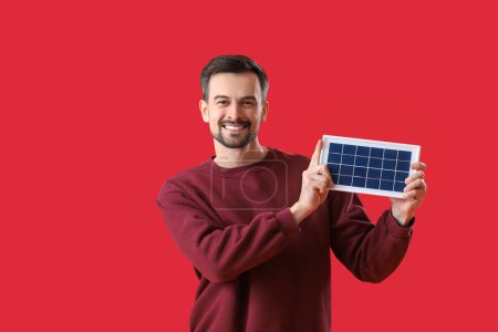 Foto de Hombre guapo con panel solar portátil sobre fondo rojo - Imagen libre de derechos