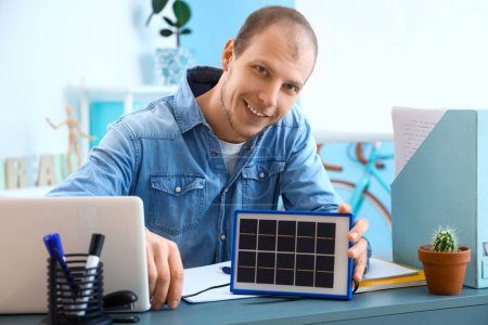 Foto de Hombre joven cargando portátil con panel solar portátil en la oficina - Imagen libre de derechos