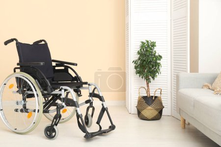 Foto de Silla de ruedas vacía con pantalla plegable, planta y sofá en el salón - Imagen libre de derechos