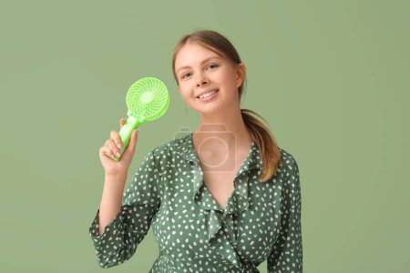 Foto de Hermosa mujer joven con mini ventilador de mano sobre fondo verde - Imagen libre de derechos