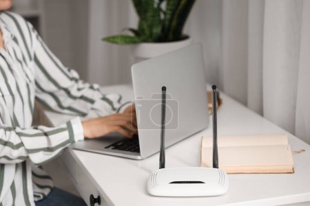 Moderner WLAN-Router auf dem Tisch der arbeitenden Frau mit Laptop, Nahaufnahme