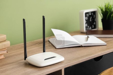 Modern wi-fi router on table near green wall in office