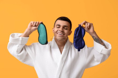Photo for Portrait of handsome young man in bathrobe with different sleeping masks on yellow background - Royalty Free Image