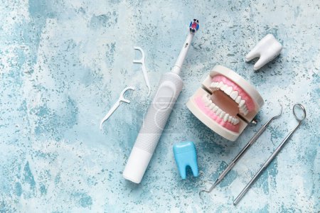 Foto de Modelo de mandíbula, herramientas dentales, cepillo de dientes y palillos de hilo dental sobre fondo azul. Día Mundial del Dentista - Imagen libre de derechos