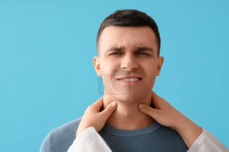 Photo for Endocrinologist examining thyroid gland of young man on blue background, closeup - Royalty Free Image