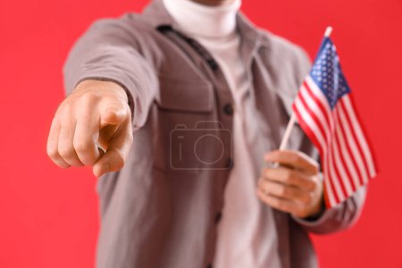 Junger Mann mit USA-Fahne zeigt auf Zuschauer auf rotem Hintergrund, Nahaufnahme. Anschuldigungskonzept