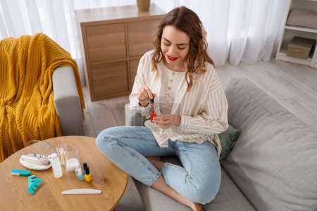 Foto de Hermosa joven con botellas de esmalte de uñas y suministros para la manicura sentado en la sala de estar - Imagen libre de derechos
