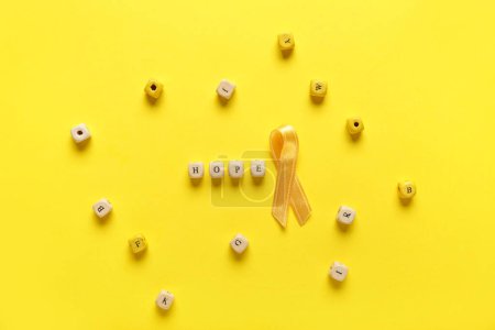 Téléchargez les photos : Ruban doré avec mot ESPOIR sur fond jaune. Concept de sensibilisation au cancer chez l'enfant - en image libre de droit