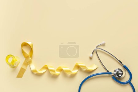 Téléchargez les photos : Ruban doré avec sucette et stéthoscope sur fond jaune. Concept de sensibilisation au cancer chez l'enfant - en image libre de droit