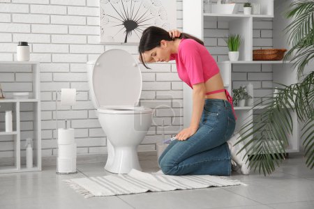Téléchargez les photos : Jeune femme malade avec test de grossesse près de cuvette de toilette dans les toilettes - en image libre de droit