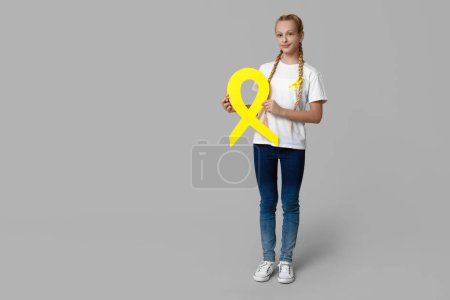 Téléchargez les photos : Adolescente avec ruban jaune sur fond gris. Journée internationale du cancer chez les enfants - en image libre de droit