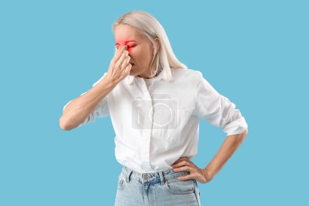 Téléchargez les photos : Femme mûre avec douleur dans le nez sur fond bleu clair - en image libre de droit
