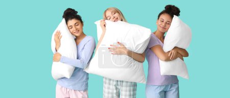 Téléchargez les photos : Belles jeunes femmes en pyjama et avec des oreillers sur fond turquoise - en image libre de droit