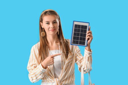 Foto de Mujer bastante joven señalando el panel solar portátil sobre fondo azul - Imagen libre de derechos