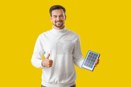 Foto de Hombre guapo con panel solar portátil que muestra el pulgar hacia arriba sobre fondo amarillo - Imagen libre de derechos