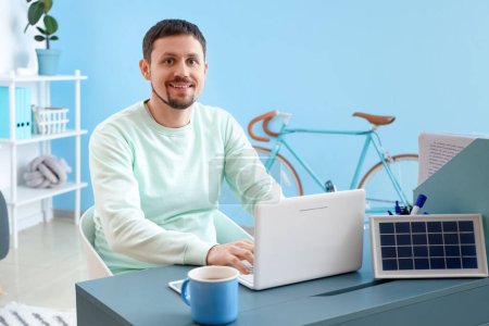 Foto de Hombre guapo usando el ordenador portátil y el panel solar portátil en la mesa en la oficina - Imagen libre de derechos