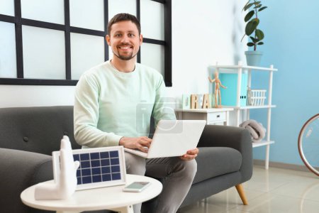 Foto de Hombre guapo usando el ordenador portátil y el panel solar portátil en la mesa en casa - Imagen libre de derechos