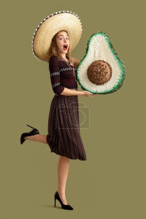 Téléchargez les photos : Jeune femme surprise en chapeau sombrero avec pinata sur fond vert. Célébration de la fête des morts au Mexique (El Dia de Muertos) - en image libre de droit