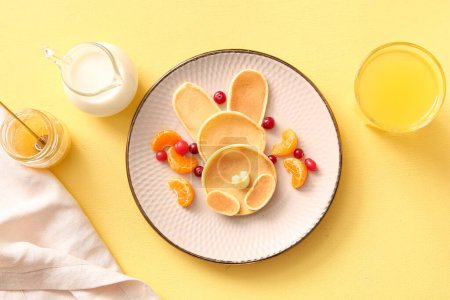 Téléchargez les photos : Crêpes de lapin de Pâques drôle avec verre de jus d'orange sur fond jaune - en image libre de droit