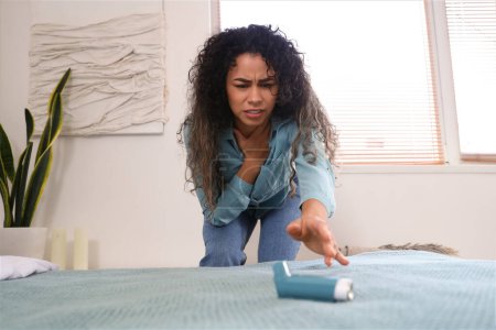 Téléchargez les photos : Jeune femme afro-américaine avec crise d'asthme prenant inhalateur du lit dans la chambre - en image libre de droit