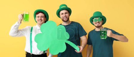 Photo for Happy young men in leprechaun's hats, with beer and clover on yellow background. St. Patrick's Day celebration - Royalty Free Image